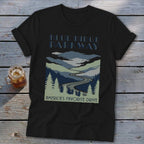 A black t-shirt with a blue graphic of the Blue Ridge Parkway and a glass of iced tea on a wooden table.