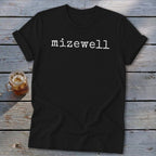Black t-shirt with white "mizewell" text, laid on wooden planks with a drink.