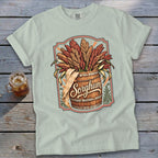 Light blue t-shirt with a graphic of sorghum stalks overflowing from a wooden barrel.