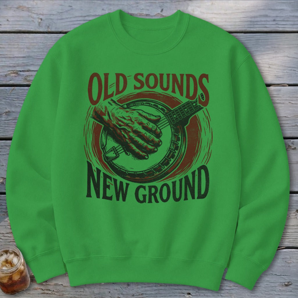 A green crewneck sweatshirt featuring a graphic of hands playing a banjo with the text Old Sounds New Ground.