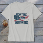 A light gray V-neck t-shirt with a distressed graphic reading New York Raised American Made over a stylized American flag design.