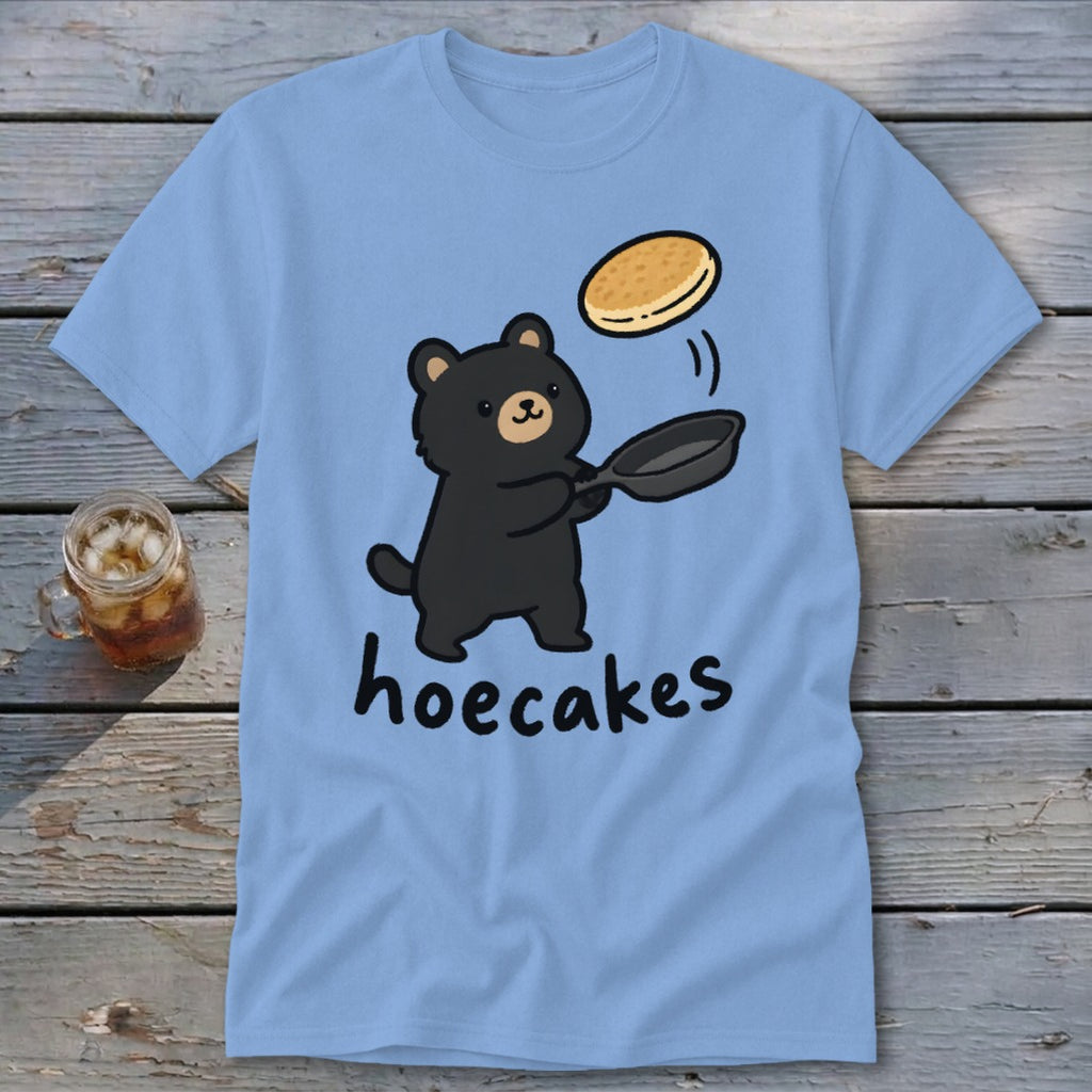 Light blue t-shirt featuring a cartoon black bear flipping a pancake with the text hoecakes.
