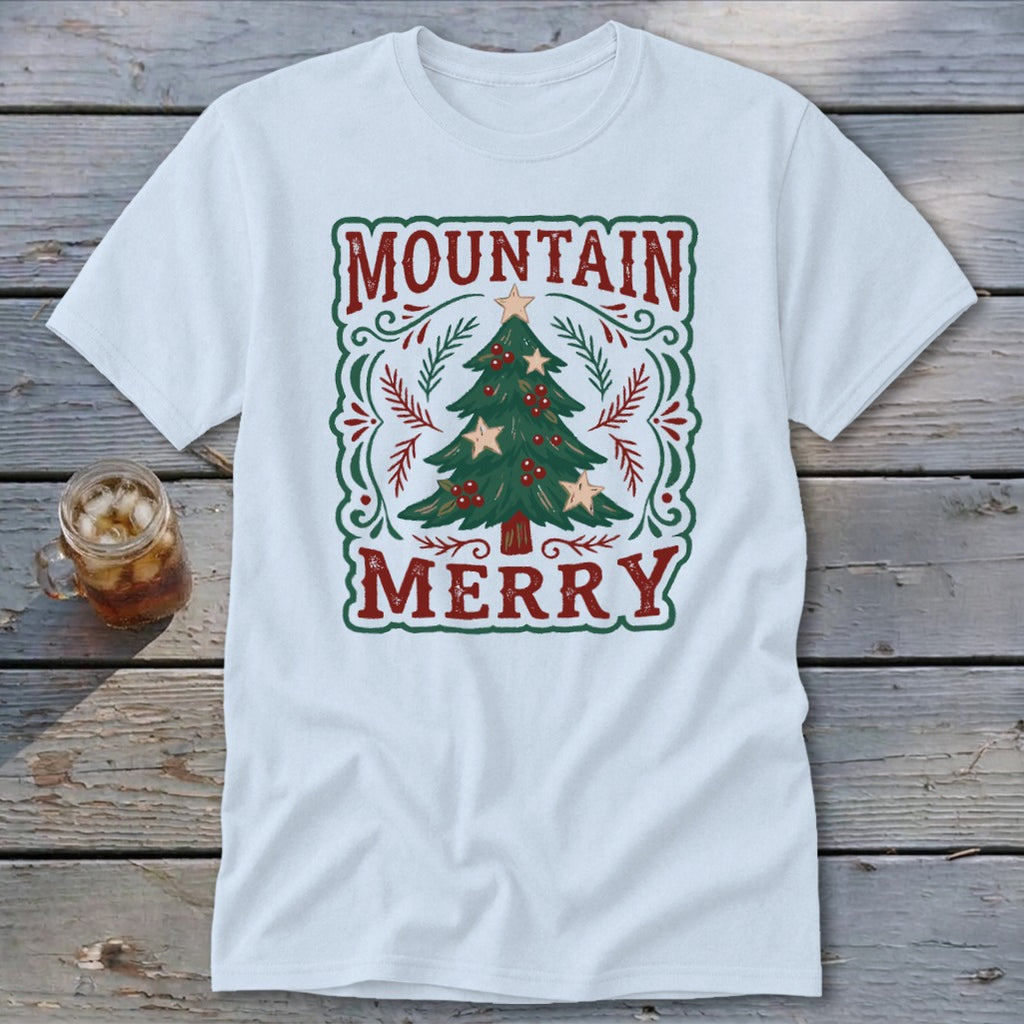 A white t-shirt features a vintage-style Christmas design with the text Mountain Merry framing a decorated tree.