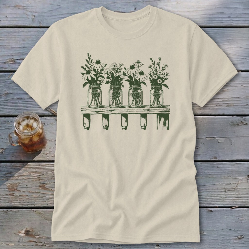 A cream-colored short-sleeved t-shirt features a green graphic of four mason jars filled with wildflowers on a shelf.