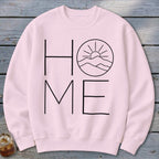 Light pink crewneck sweatshirt featuring a black graphic with the word HOME, where the O is replaced by a mountain and sun design.