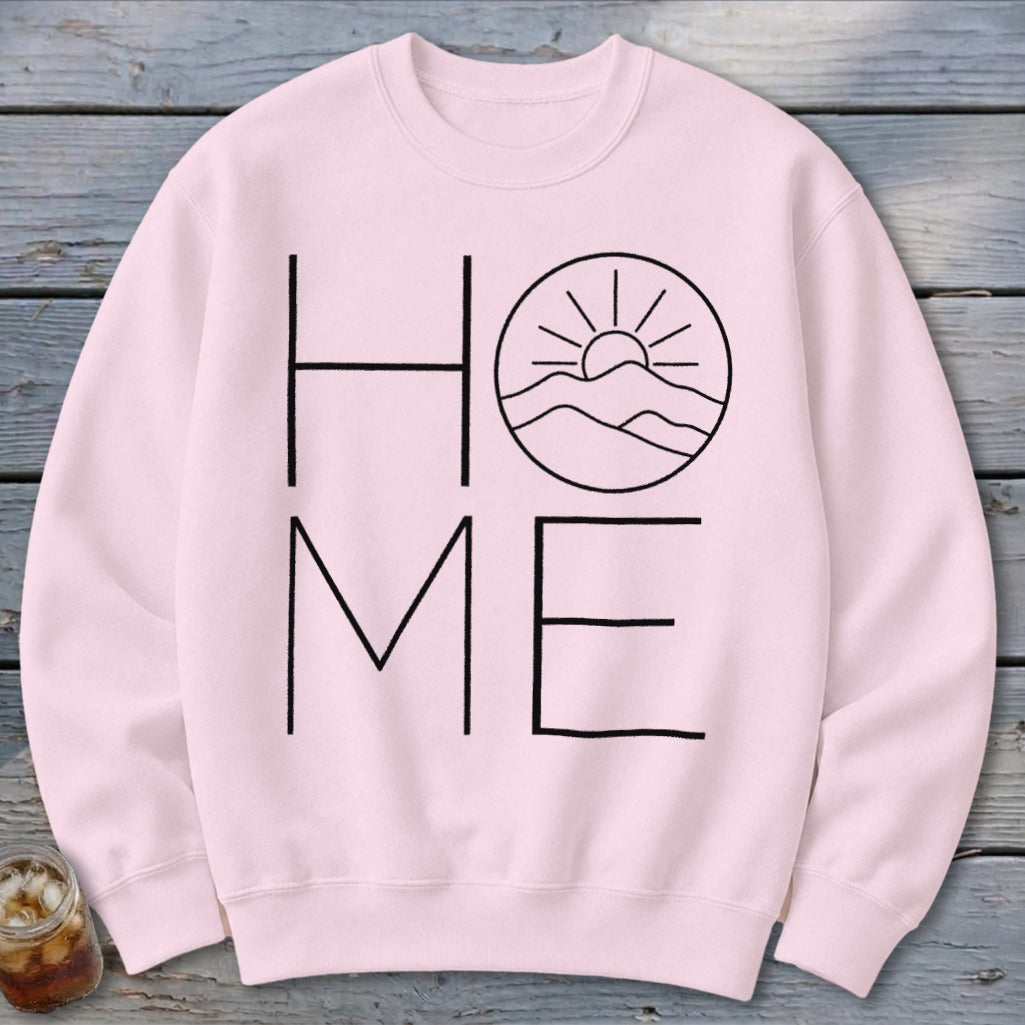 Light pink crewneck sweatshirt featuring a black graphic with the word HOME, where the O is replaced by a mountain and sun design.