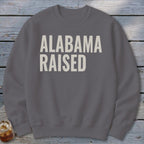 Gray sweatshirt with cream text that reads "ALABAMA RAISED".