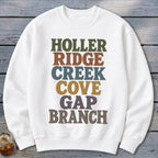 A white crewneck sweatshirt features colorful block lettering spelling out HOLLER RIDGE CREEK COVE GAP BRANCH.