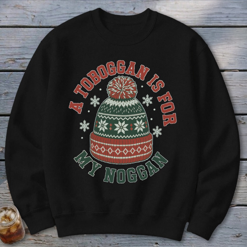 A black crewneck sweatshirt featuring a graphic of a winter knit hat surrounded by snowflakes and the text A TOBOGGAN IS FOR MY NOGGAN.