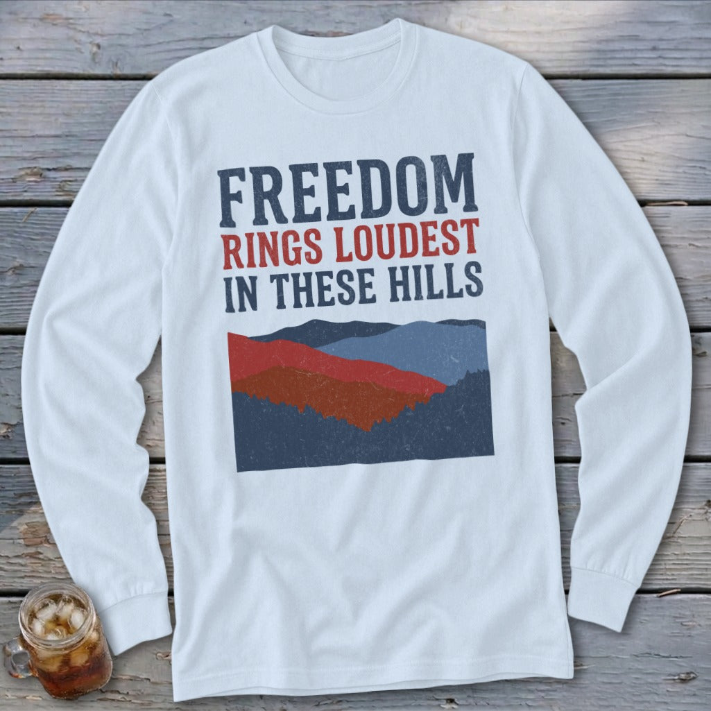 White long-sleeve t-shirt with the text FREEDOM RINGS LOUDEST IN THESE HILLS above a mountain illustration.