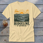 Light yellow t-shirt with "RIDGELINE AT DAYBREAK" text and mountain landscape graphic.
