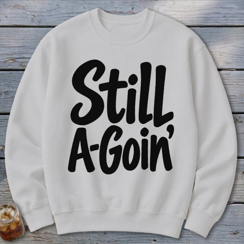 A white crewneck sweatshirt featuring the black bold text Still A-Goin' centered on the chest.