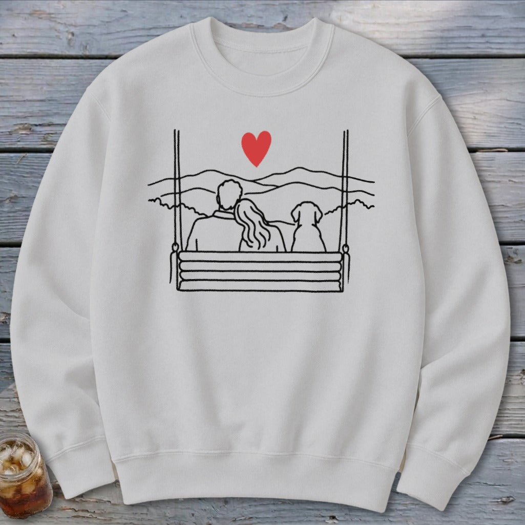 White sweatshirt with line drawing of couple and dog on a swing with a heart.