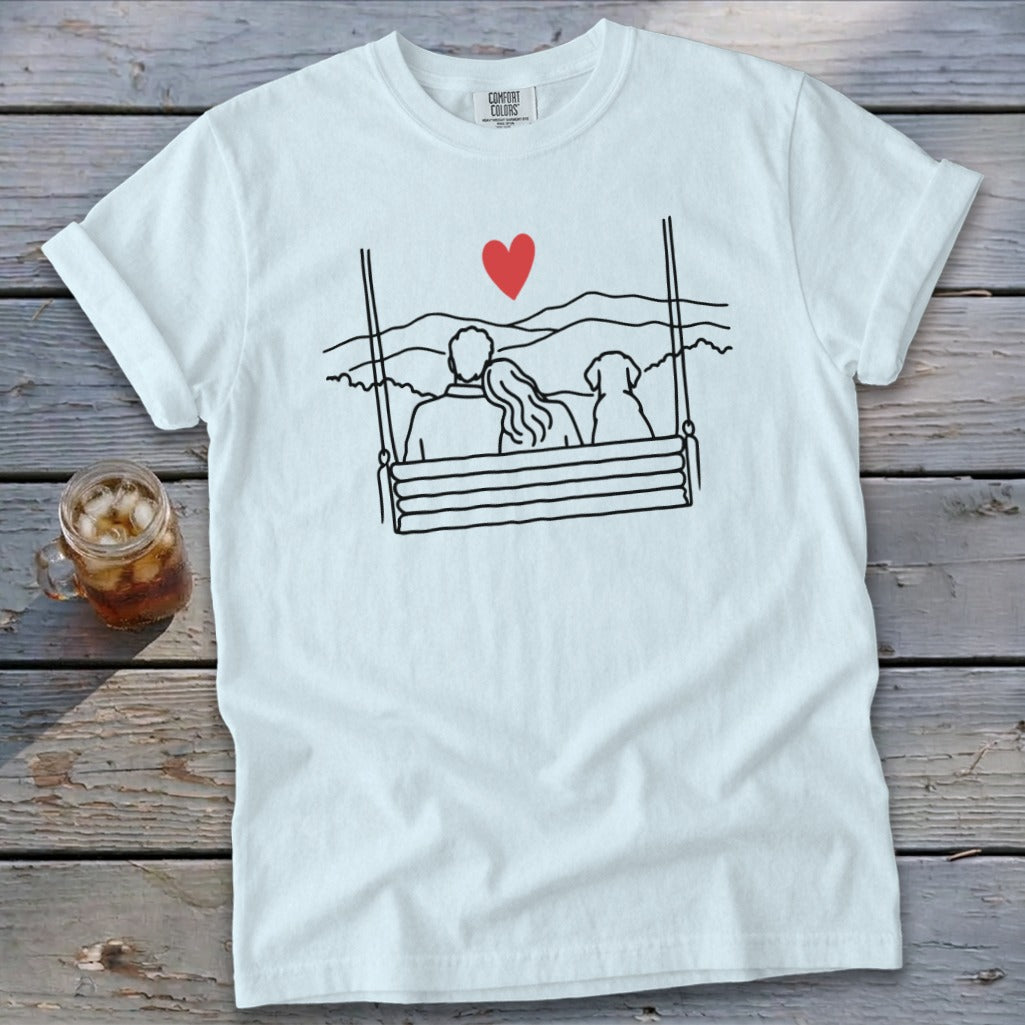 White t-shirt with black line art of couple and dog on swing, red heart above.