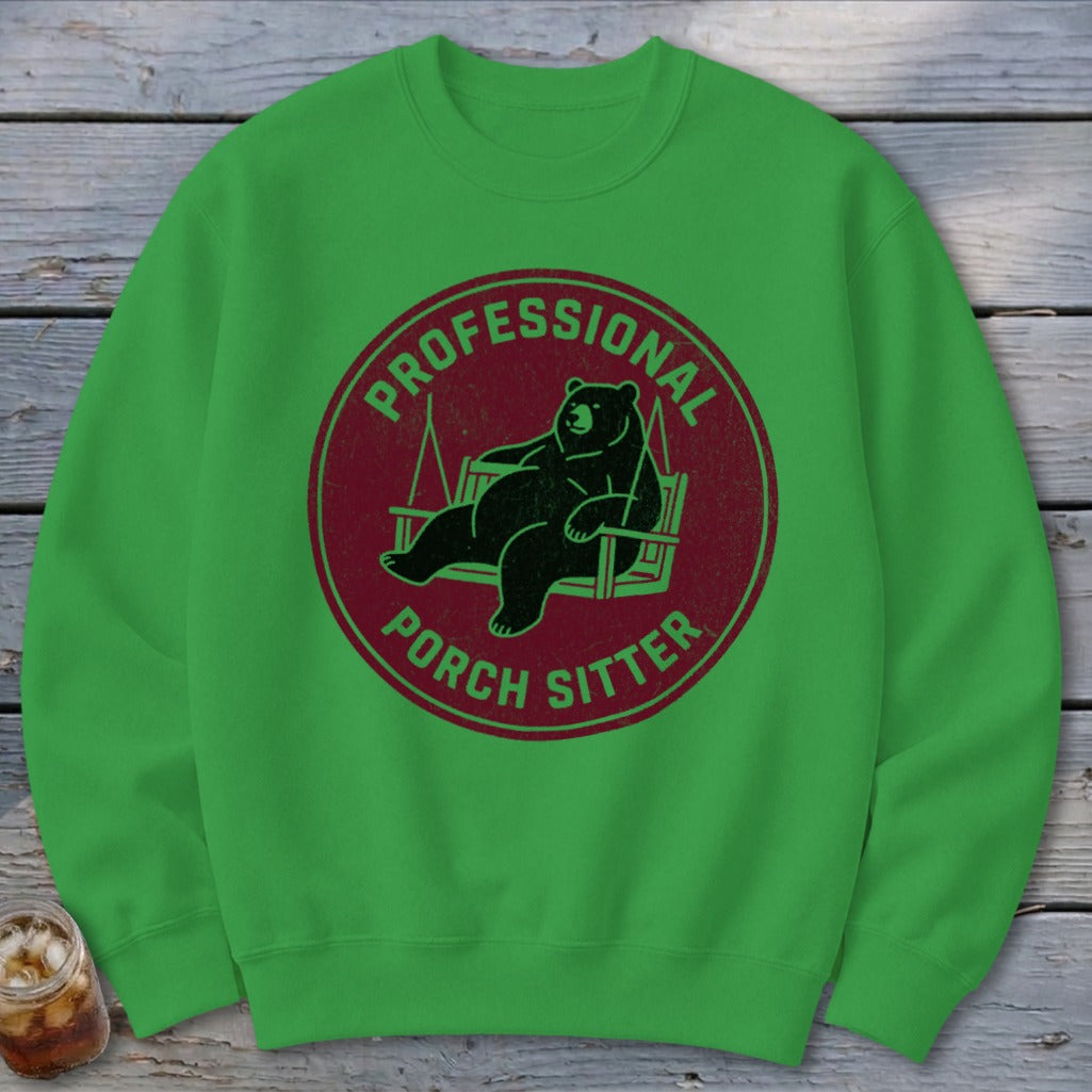 Bright green crewneck sweatshirt featuring a circular maroon graphic of a bear lounging on a porch swing with text reading Professional Porch Sitter.