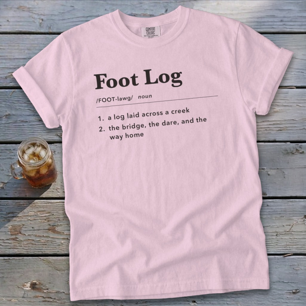 Light pink t-shirt featuring black dictionary-style text defining the term Foot Log on a wooden background.