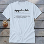A light blue t-shirt printed with a dictionary definition of Appalachia rests on a wooden surface beside a small jar of iced tea.