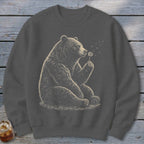 Bear sitting and blowing on a dandelion on a dark gray sweatshirt.