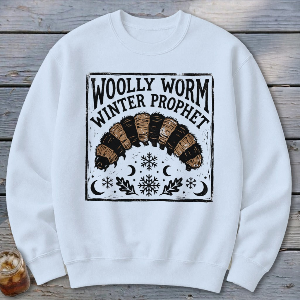 A white crewneck sweatshirt featuring a black graphic of a woolly worm with text reading Woolly Worm Winter Prophet.