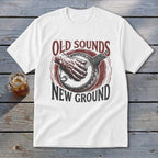A white t-shirt featuring a graphic print of a hand playing a banjo and text that reads Old Sounds New Ground.