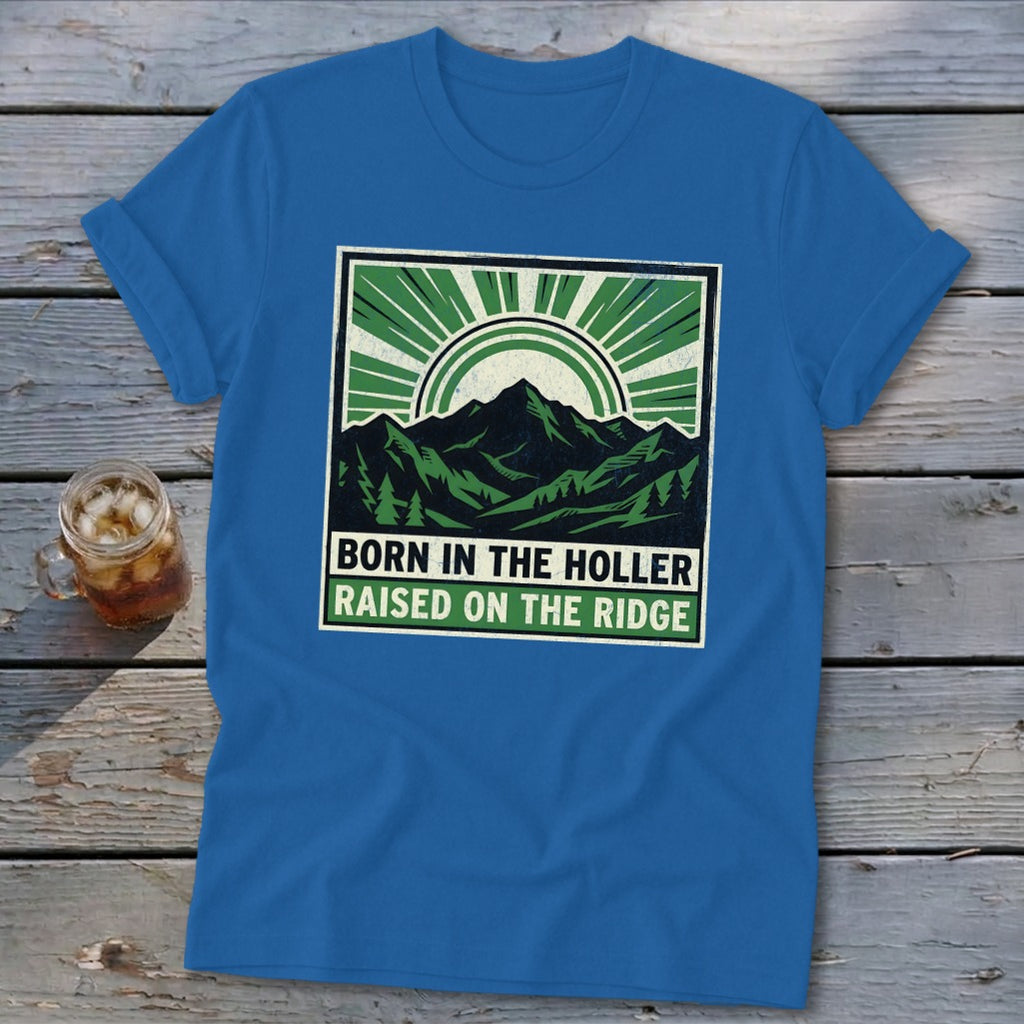 Blue t-shirt featuring a green and black graphic of mountains, sunshine, and the text Born in the Holler, Raised on the Ridge.