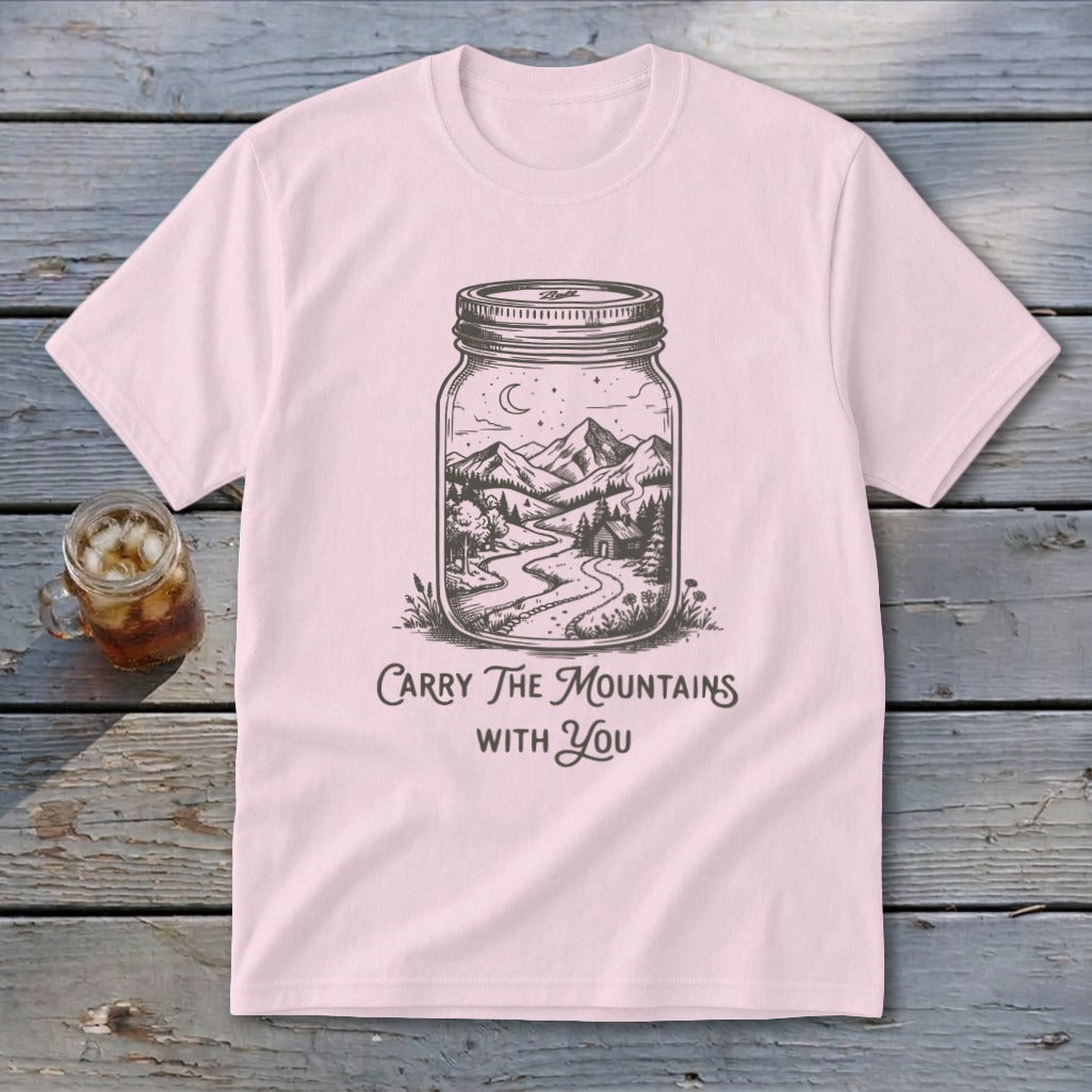 A pink short-sleeve t-shirt with a graphic of mountains and a cabin inside a mason jar and text reading Carry The Mountains With You.