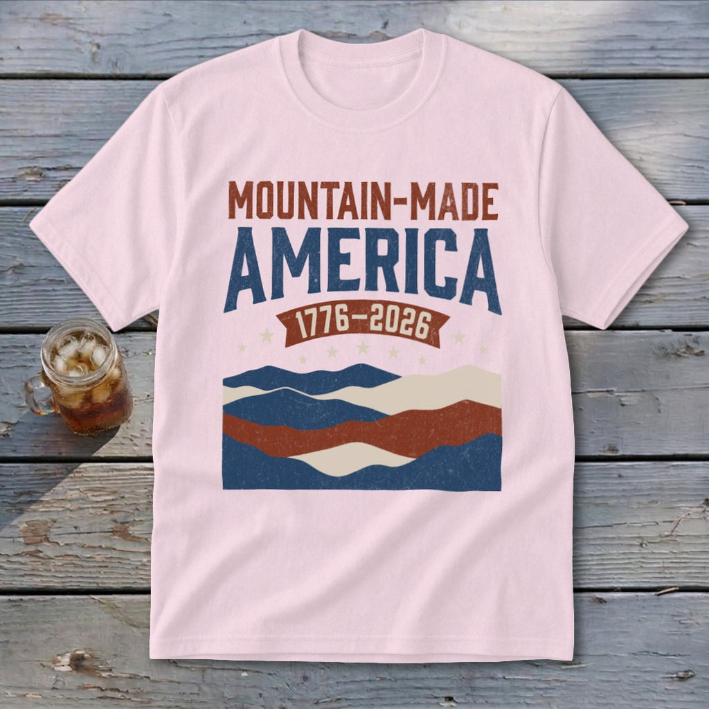 Light pink t-shirt featuring mountain graphic and text reading MOUNTAIN-MADE AMERICA 1776-2026.