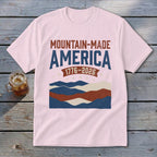 Light pink t-shirt featuring mountain graphic and text reading MOUNTAIN-MADE AMERICA 1776-2026.