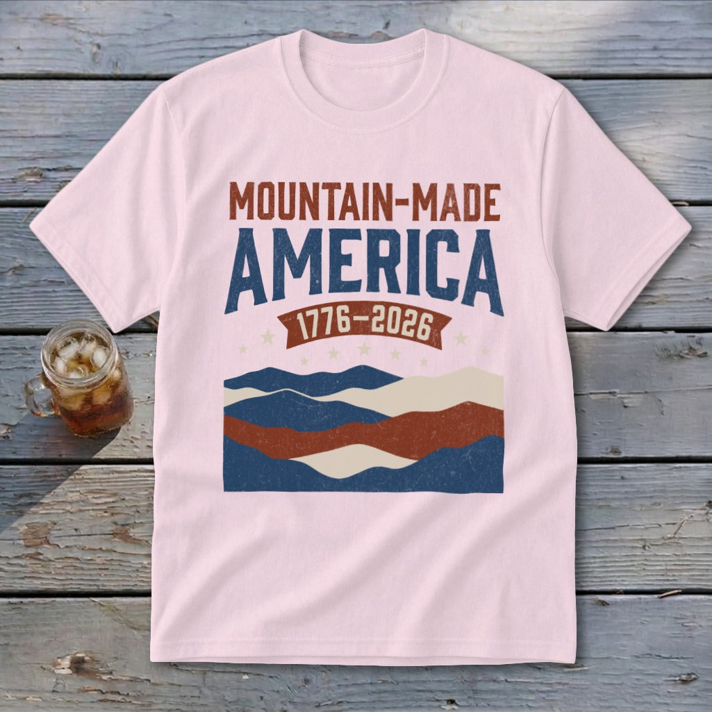 Light pink t-shirt featuring mountain graphic and text reading MOUNTAIN-MADE AMERICA 1776-2026.