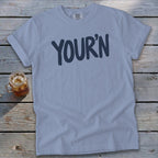 Light blue t-shirt with "YOUR'N" graphic and a glass of iced tea.