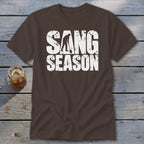 A brown t-shirt featuring white distressed text reading "SANG SEASON" with a silhouette of a person digging.