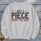 White sweatshirt with "JUST A PIECE DOWN THE ROAD" graphic text.