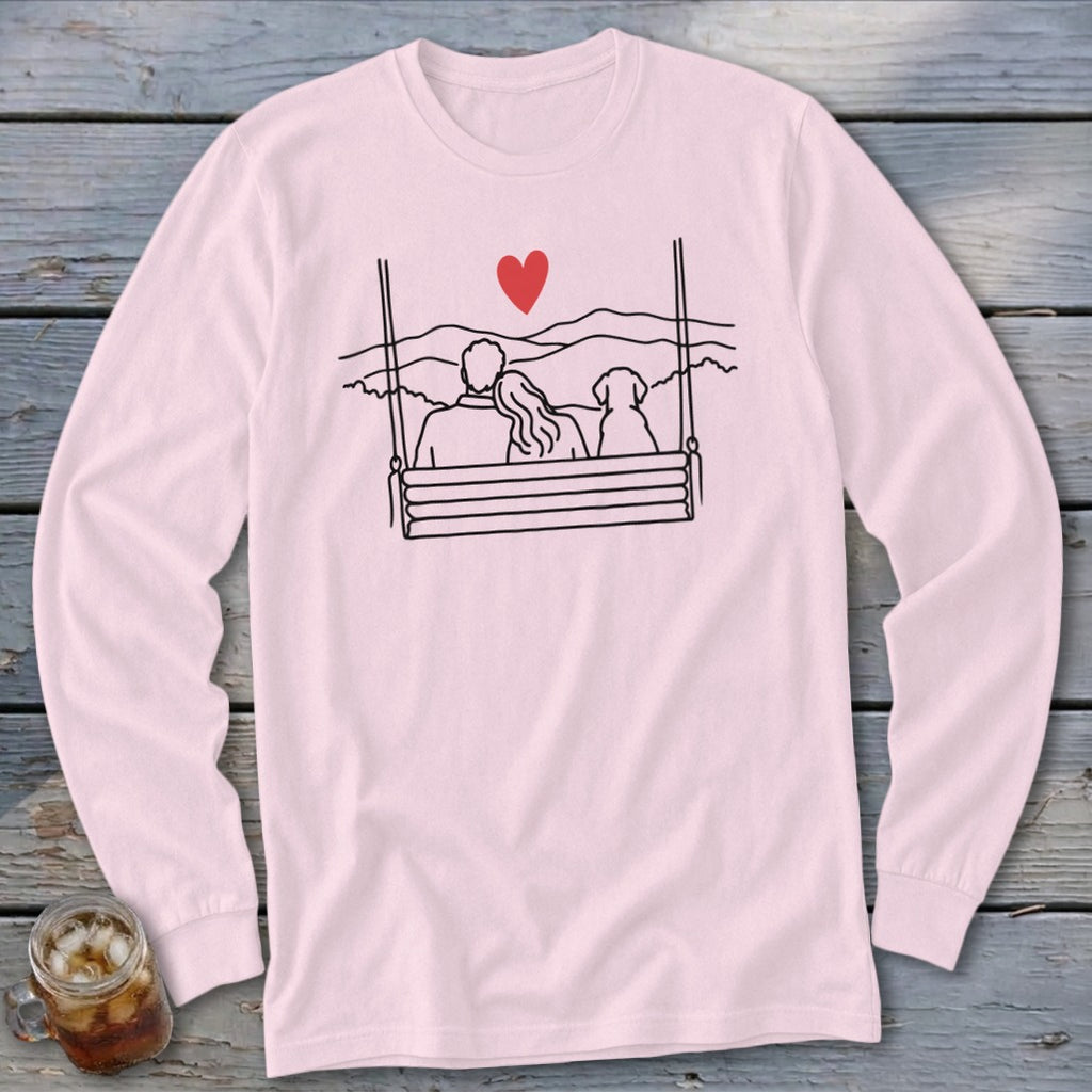 Couple and dog on a swing with heart and mountains graphic on a pink long-sleeve shirt.