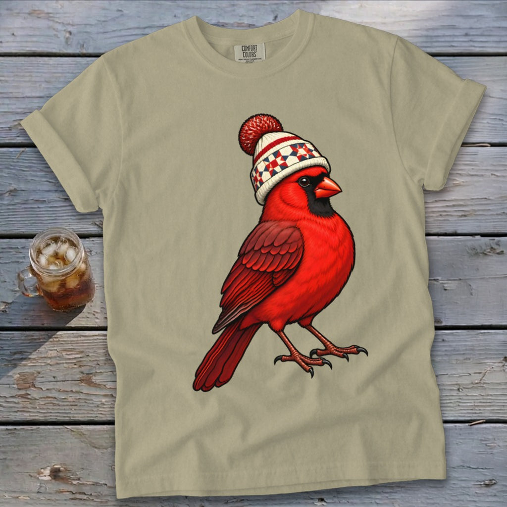 Light olive green crewneck t-shirt featuring a red cardinal wearing a winter beanie, laid on a wooden background.