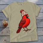Light olive green crewneck t-shirt featuring a red cardinal wearing a winter beanie, laid on a wooden background.
