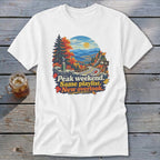 White t-shirt graphic with autumn mountain scene and text "Peak weekend. Same playlist. New overlook."