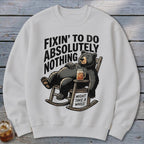 Off-white crewneck sweatshirt featuring a black bear lounging in a rocking chair with text reading FIXIN TO DO ABSOLUTELY NOTHING MIGHT TAKE A WHILE.