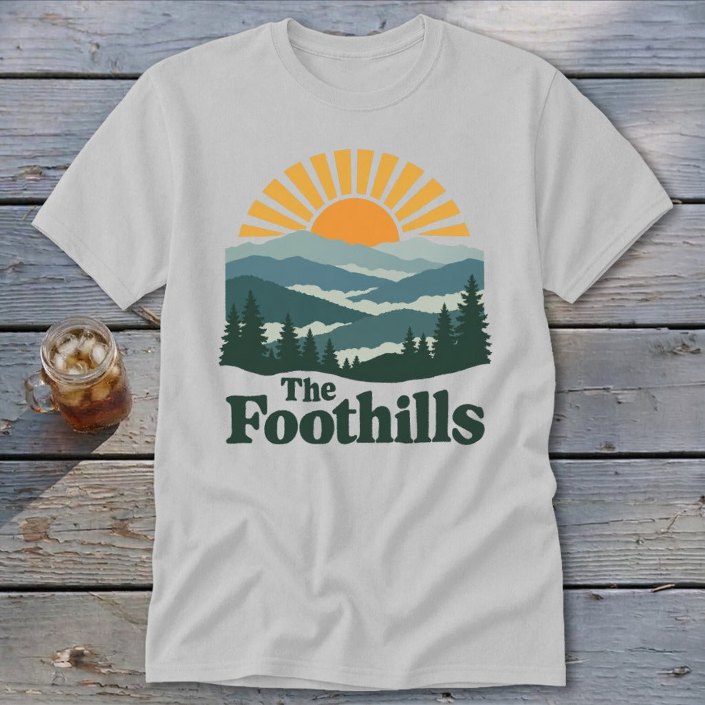 White t-shirt with sunset mountain range graphic and "The Foothills" text.