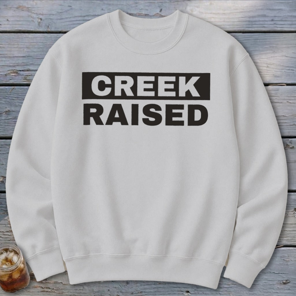 White crewneck sweatshirt with black text "CREEK RAISED"