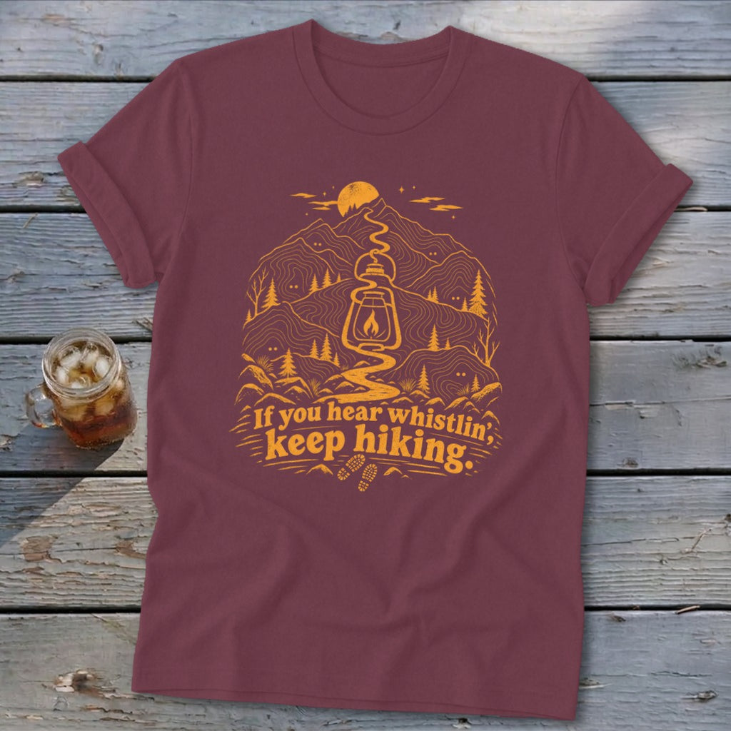 Maroon t-shirt with orange mountain graphic and "If you hear whistlin', keep hiking" text.