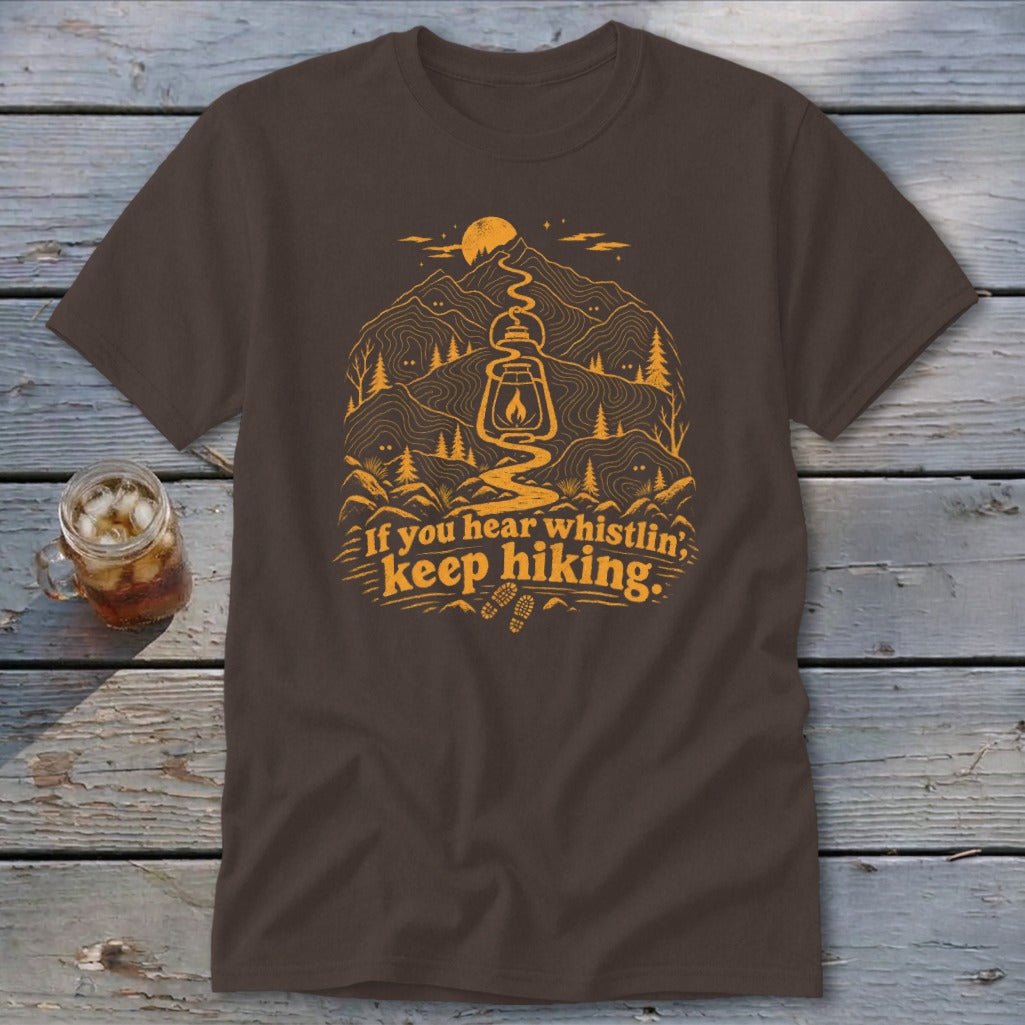 Brown t-shirt with "If you hear whistlin', keep hiking." text and mountain graphic.