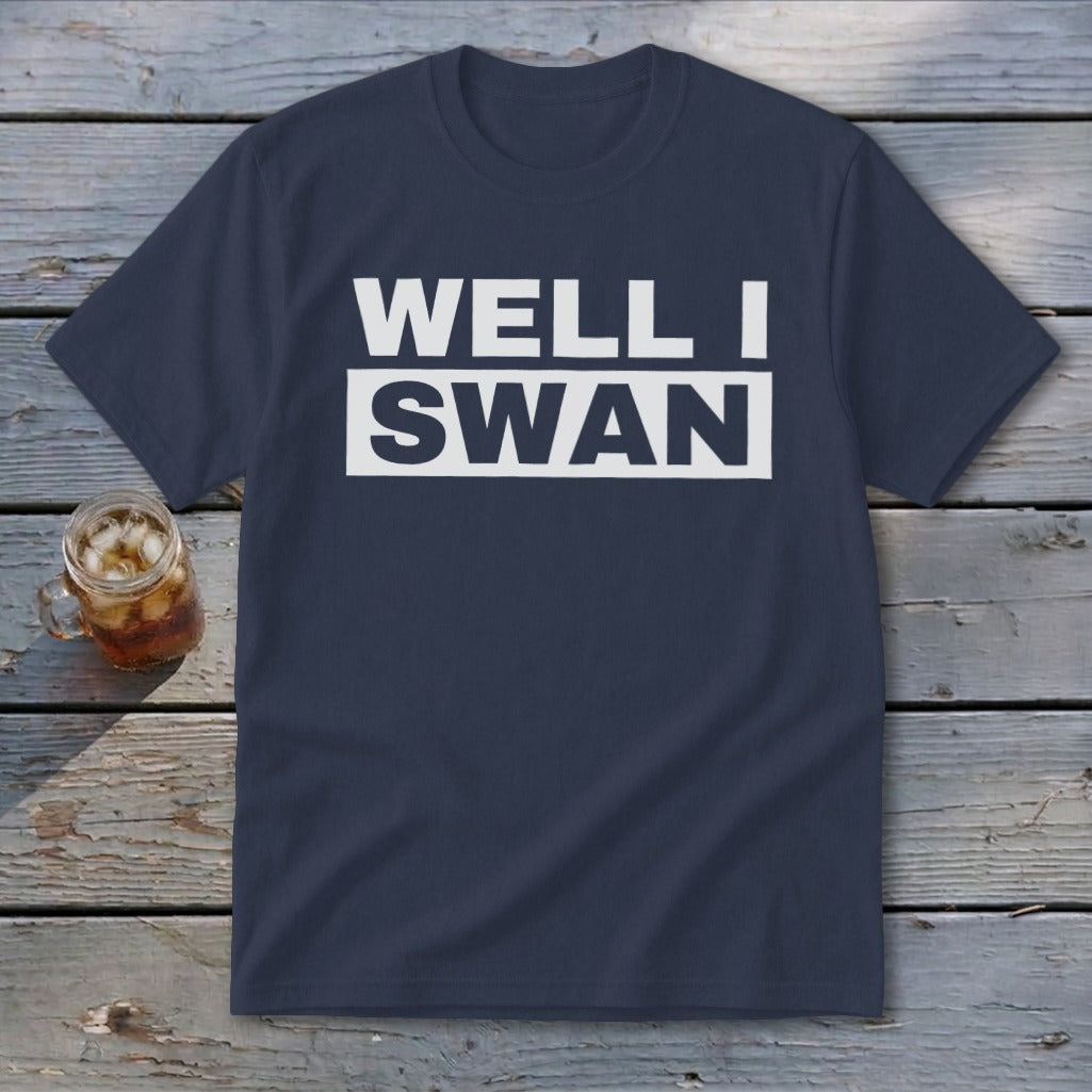 A dark blue t-shirt with white text that reads WELL I SWAN on a wooden background.