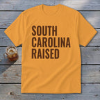 Orange t-shirt with brown text "SOUTH CAROLINA RAISED".