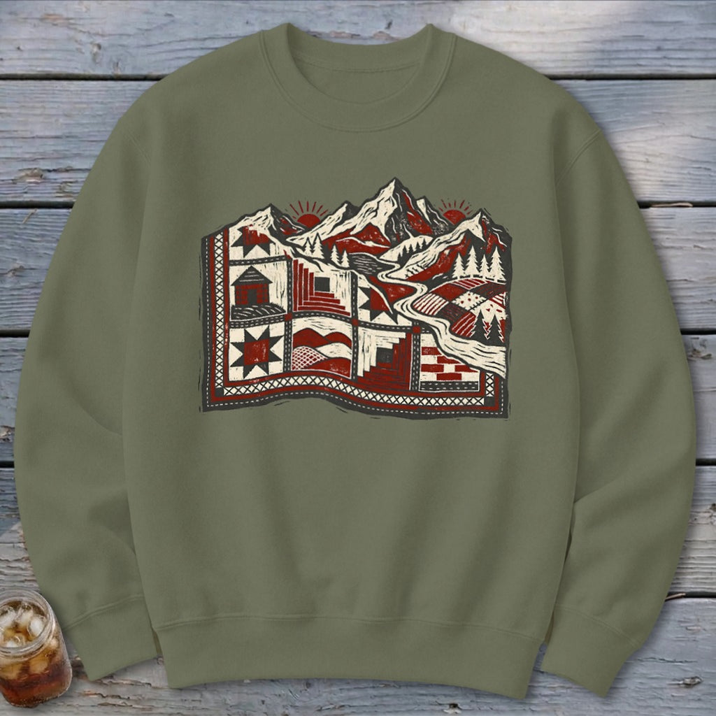 An olive green crewneck sweatshirt featuring a graphic of mountains and a quilted landscape.