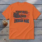 An orange t-shirt featuring the text Pennsylvania Raised American Made and a distressed American flag graphic.