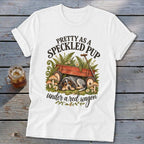 White t-shirt with a speckled pup sleeping under a red wagon and ferns.