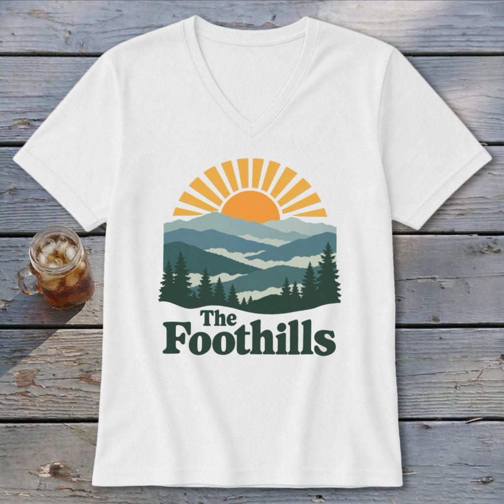 White v-neck t-shirt with graphic of sun setting over layered mountains and trees, reading "The Foothills".