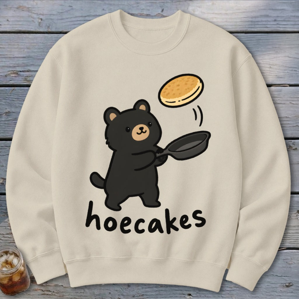 Beige sweatshirt featuring a cute black bear flipping a pancake in a pan, with the text hoecakes.