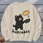 Beige sweatshirt featuring a cute black bear flipping a pancake in a pan, with the text hoecakes.