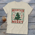 Beige t-shirt featuring a green Christmas tree graphic, red berries, stars, and the text MOUNTAIN MERRY.